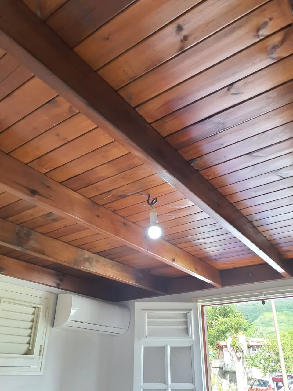 Ampoule nue sous un plafond en lambris de bois verni avant la pose d'un brasseur FANELITE au Vauclin
